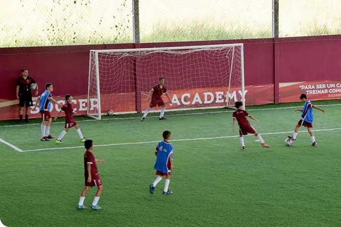 Atletas da Belletti Soccer Academy em jogo, disputando a bola perto do gol